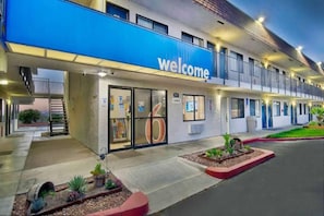Un hotel con un letrero de 'Welcome', una entrada cubierta y un estacionamiento con jardines.