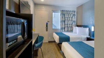 A hotel room with a television, two beds, a desk, and a window.