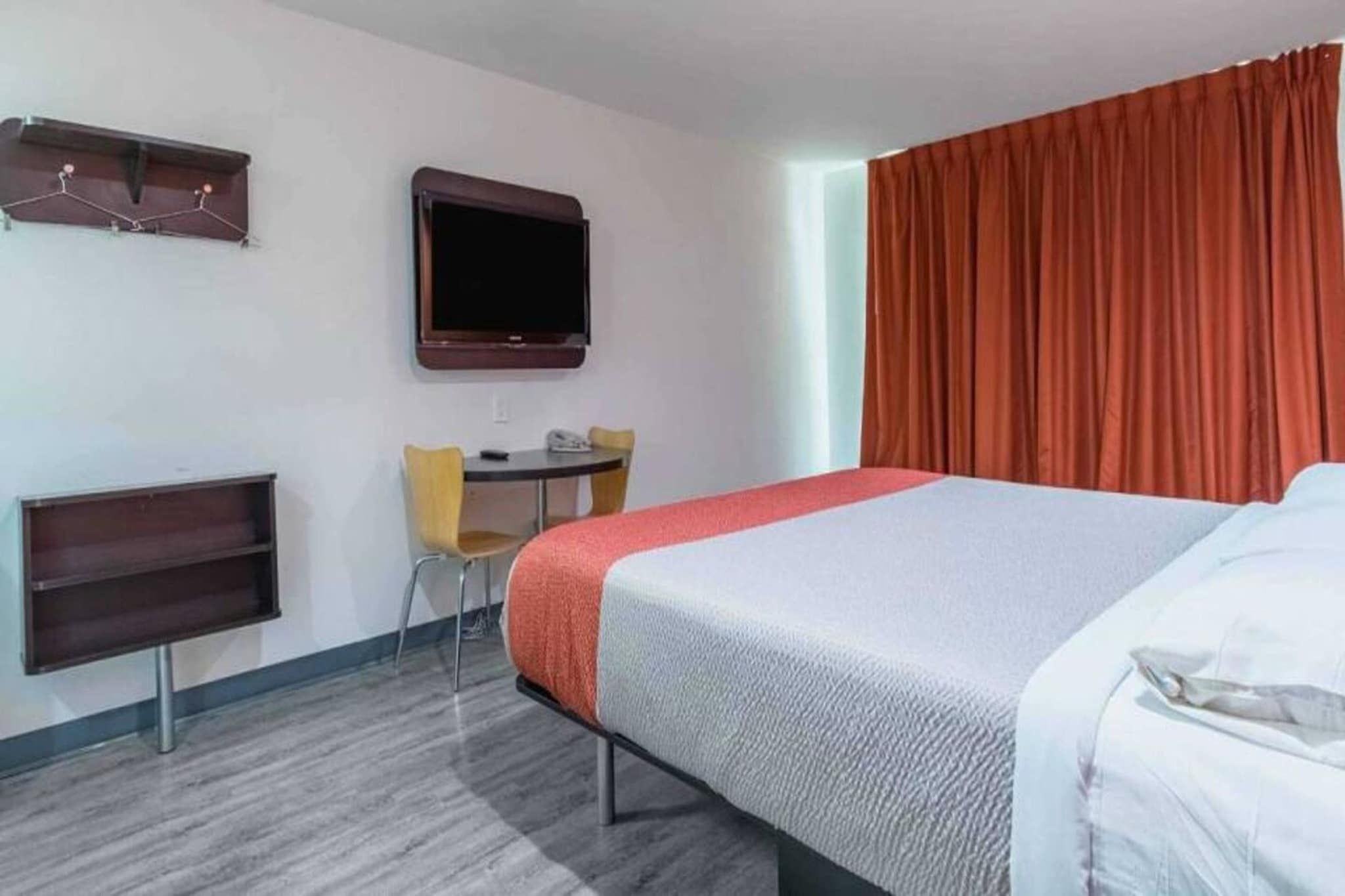 Ein Hotelzimmer mit Bett, Schreibtisch mit Stuhl, Fernseher und einem Fenster mit Vorhängen.
