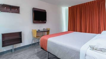 A hotel room with a bed, a desk with a chair, a television, and a window with curtains.