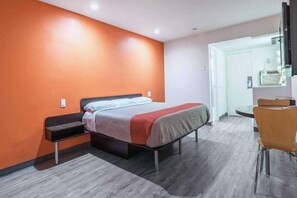 A hotel room with a bed, a desk, and a chair. - 1 King Bed | Non-Smoking (BARSTOW)