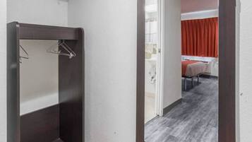 A hotel corridor with a wooden wardrobe, a bathroom with a shower, and a bed with red curtains.