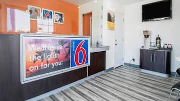 A hotel reception area with a large sign, a flat-screen TV, a coffee machine, and a counter.