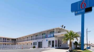 A motel with a 'NOW OPEN' sign, a '6' sign, and a 'WELCOME' sign.