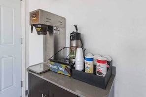 Eine Kaffeemaschine, eine Tassehalterung sowie Behälter mit Sahne und Zucker auf einer Arbeitsfläche.