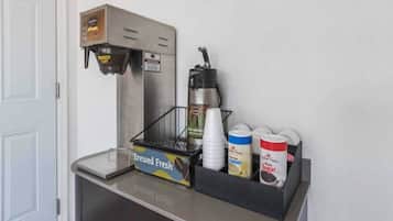 A coffee machine, a coffee cup holder, and containers of creamer and sugar on a counter.