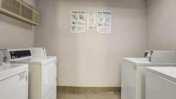 Una sala de lavandería con dos lavadoras, un secadora y dos carteles instructivos en la pared.