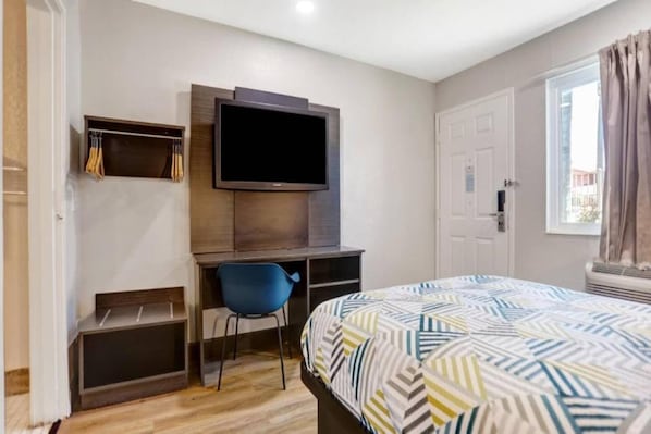 Een slaapkamer met een bed, een bureau met stoel, een televisie en een kledingkast.