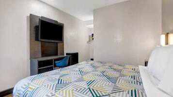 A hotel room with a bed, a desk with a chair, a flat-screen TV mounted on the wall, and a small table.
