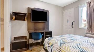 A bedroom with a bed, a desk with a chair, a television, and a wardrobe.