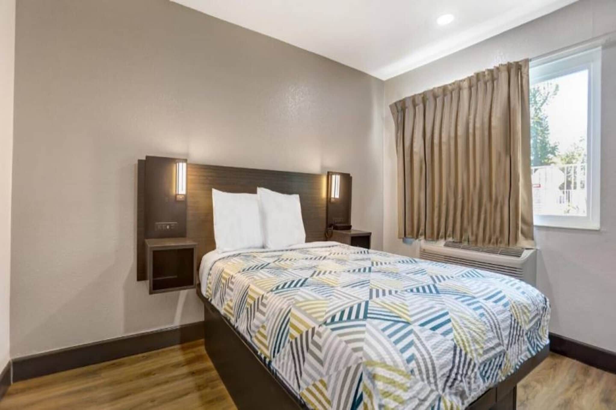 Habitación de hotel con cama, mesitas de noche, una ventana con cortinas y un equipo de aire acondicionado de pared.