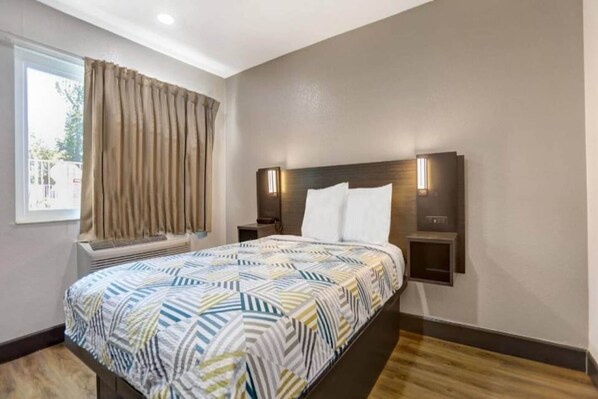 A hotel room with a bed, a window with curtains, a bedside table, and a wall-mounted light fixture.