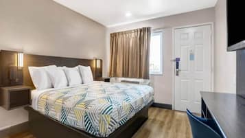 Habitación de hotel con cama, mesita de noche, televisor y ventana con cortinas.