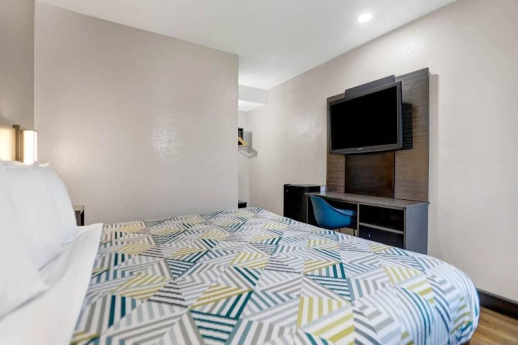 A hotel room with a bed, a desk, a chair, and a TV mounted on the wall.