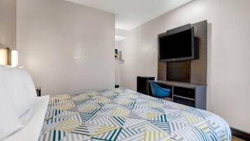 A hotel room with a bed, a desk, a chair, and a TV mounted on the wall.
