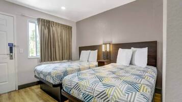 A hotel room with two beds, a window with curtains, a door, and a nightstand with a lamp.