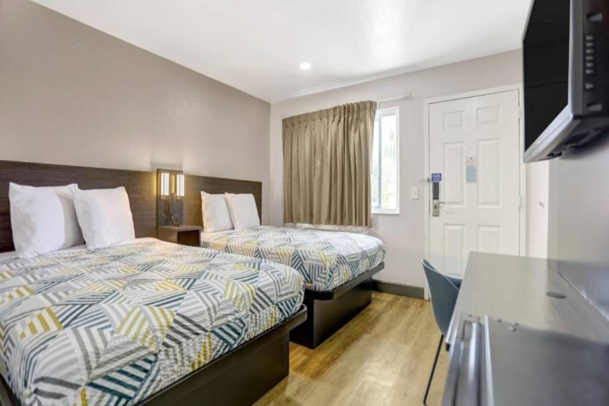 A hotel room with two beds, a desk, a television, and a window with curtains.