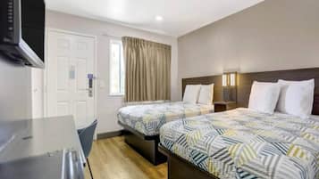 A hotel room with two beds, a desk, a television, and a window with curtains.