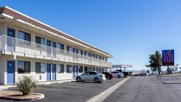 Un motel con una fila de habitaciones, un estacionamiento y un cielo azul despejado.