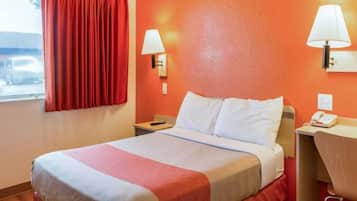 A hotel room with a bed, a nightstand, a desk, a chair, and a window with curtains.