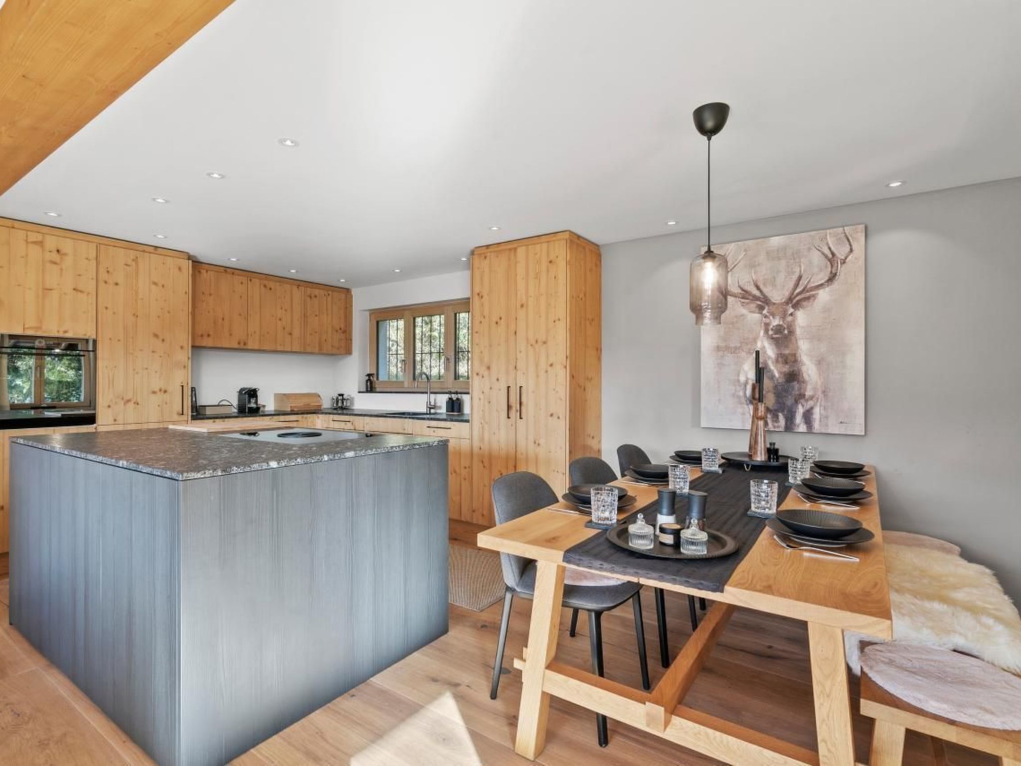 Une cuisine moderne avec des meubles en bois, un îlot central et un coin repas avec une table dressée pour quatre personnes.