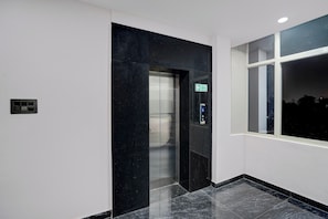 A modern elevator with a digital display, a fire exit sign, and a window with a view of the night sky. - Townhouse Vishwavidyalaya Metro Station (Kanpur)