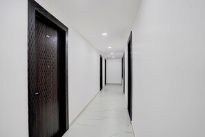 A corridor with white walls and a marble floor leading to doors with black frames and a number plate. - Townhouse Vishwavidyalaya Metro Station (Kanpur)