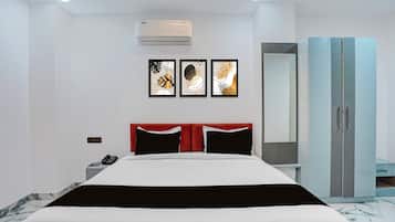 Habitación de hotel con cama, cabecera roja, armario y tres cuadros en la pared.