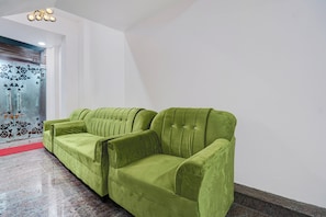A green sofa in a room with a red carpet and a glass door with floral designs. - Townhouse Vishwavidyalaya Metro Station (Kanpur)