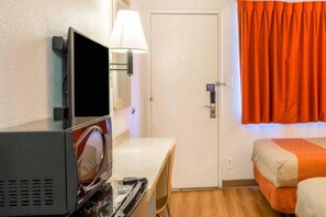 A hotel room with a bed, a desk with a computer, a television, and a door.