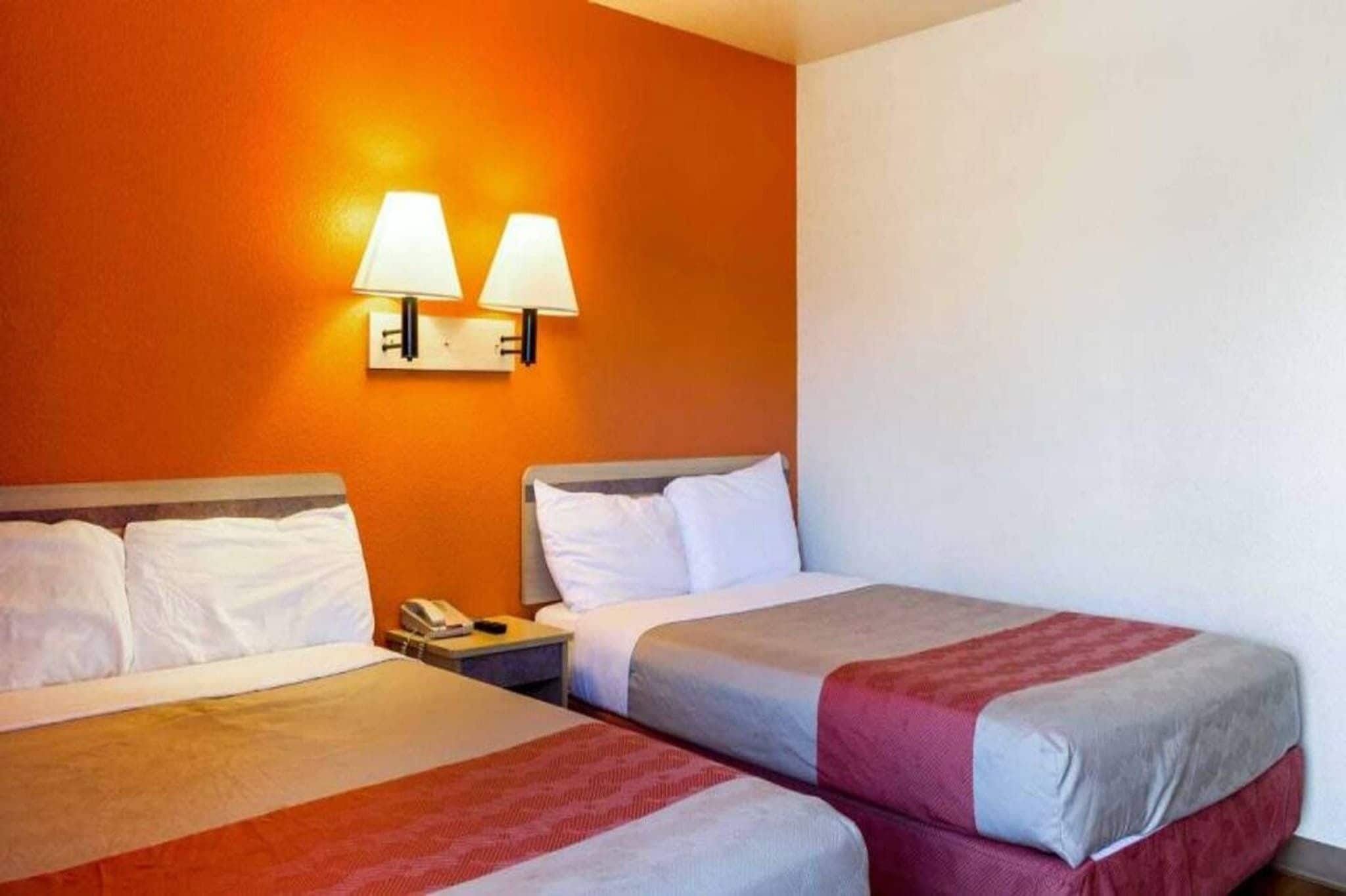 Een hotelkamer met twee bedden, een nachtkastje met een telefoon en twee wandlampen.