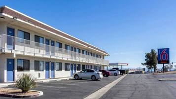 A motel with a row of rooms, a parking lot, and a clear blue sky.