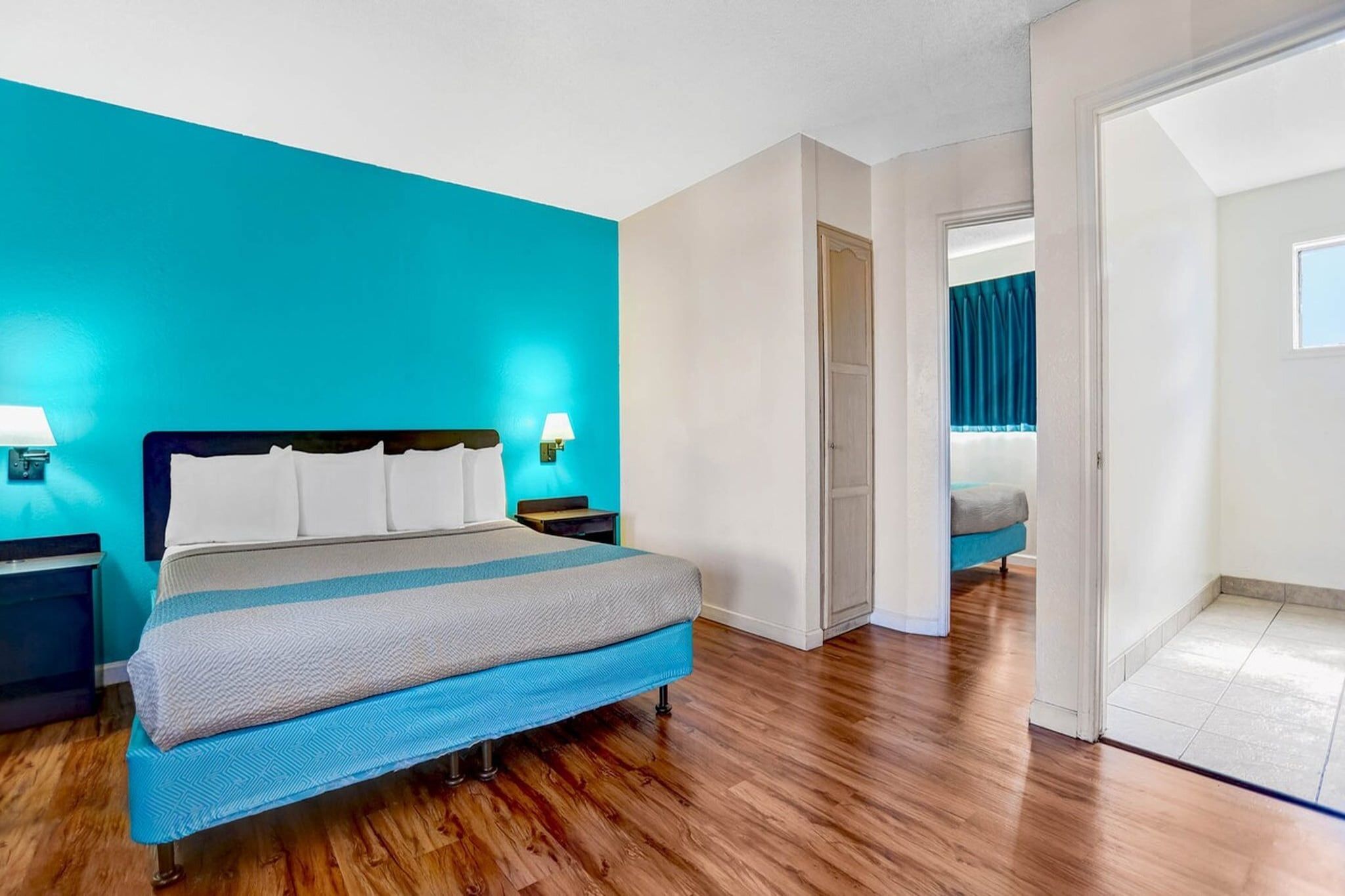 A bedroom with a bed, nightstands, a door, and a view of another room.