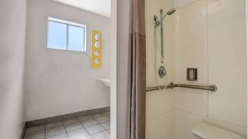 A bathroom with a shower, a window, and a wall-mounted clock.