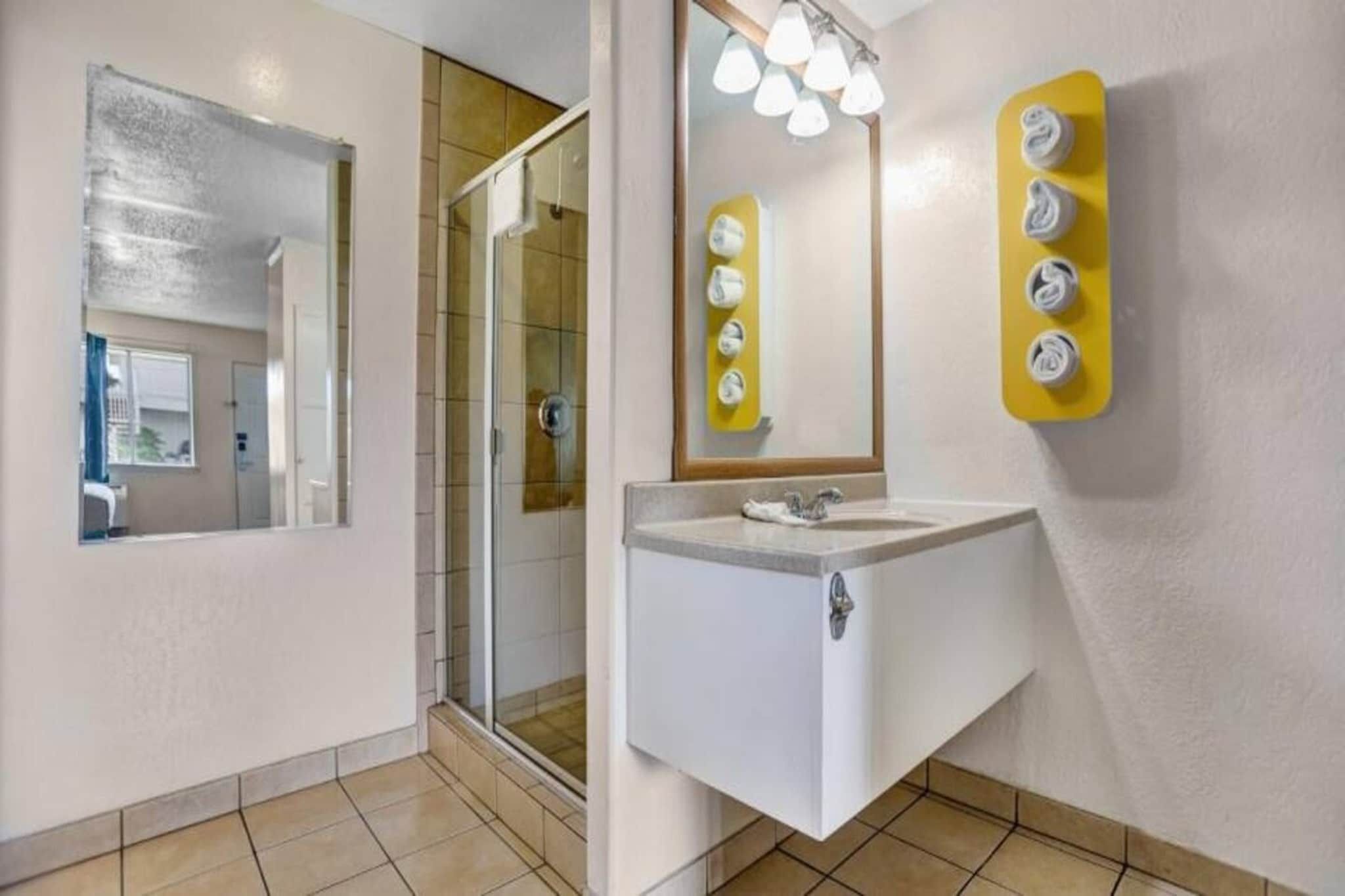 Een badkamer met een douchecabine van glas, een wastafel met spiegel en een handdoekdispenser.