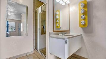 Een badkamer met een douchecabine van glas, een wastafel met spiegel en een handdoekdispenser.