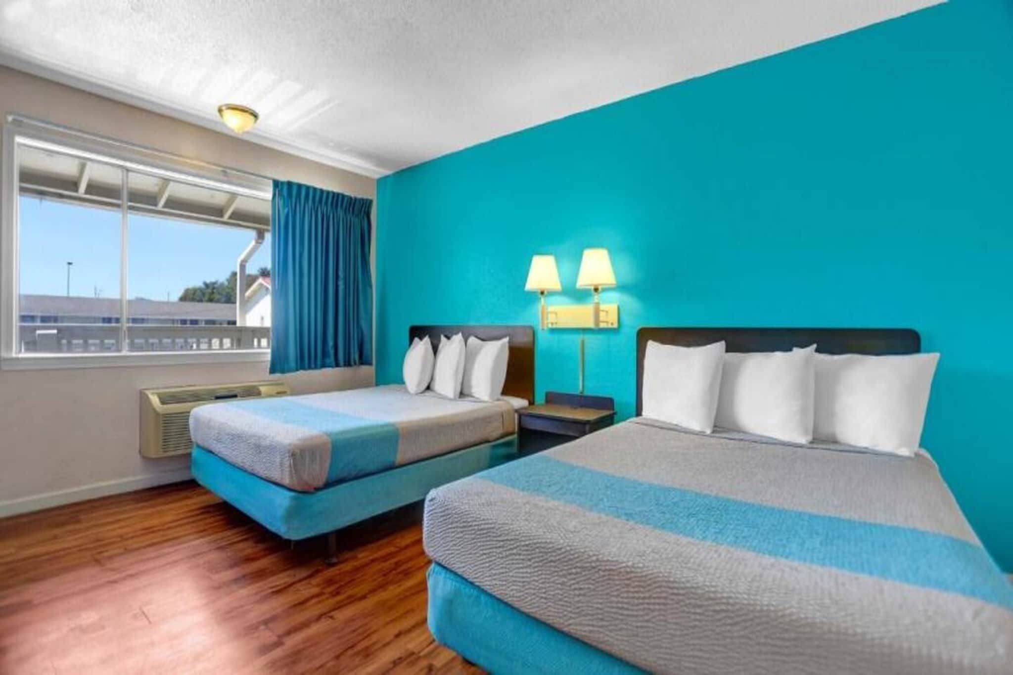 A hotel room with two beds, a large window, and a view of the outside.