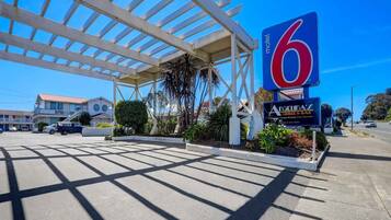 A motel with a large blue sign, a covered parking area, and a building with a red roof in the background.