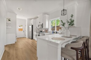 A modern kitchen with white cabinetry, a central island, and a view to the outdoors. - Designer 4BR Home with Hot tub Gated - sleep 10 (Houston)