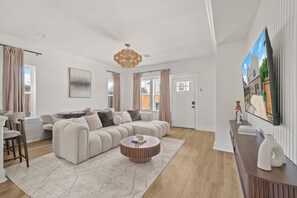 A modern living room with a sectional sofa, a round coffee table, and a flat-screen TV mounted on the wall. - Designer 4BR Home with Hot tub Gated - sleep 10 (Houston)