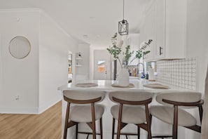 A modern kitchen with a central island, bar stools, pendant lighting, and a view into the adjacent dining area. - Designer 4BR Home with Hot tub Gated - sleep 10 (Houston)