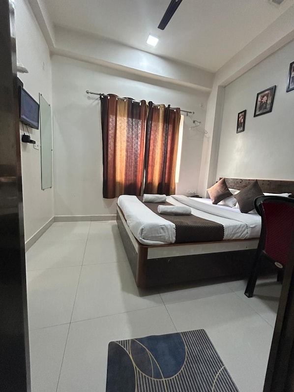 A hotel room with a bed, a desk, a chair, a TV, and curtains. - Hotel Kashi Varanasi (varanasi)
