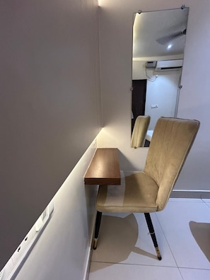 A room with a single beige chair, a small wooden table, and a white air conditioning unit mounted on the wall. - Hotel Kashi Varanasi (varanasi)