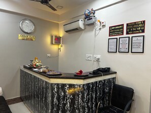 A hotel reception desk with a clock, air conditioning unit, and various informational signs. - Hotel Kashi Varanasi (varanasi)