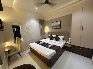 A hotel room with a bed, bedside table, nightstand, wardrobe, and a mirror. - Hotel Kashi Varanasi (varanasi)