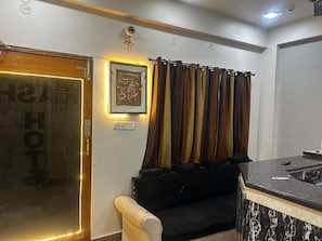 A hotel lobby with a reception desk, a sofa, a framed picture on the wall, and a door with a pull handle. - Hotel Kashi Varanasi (varanasi)