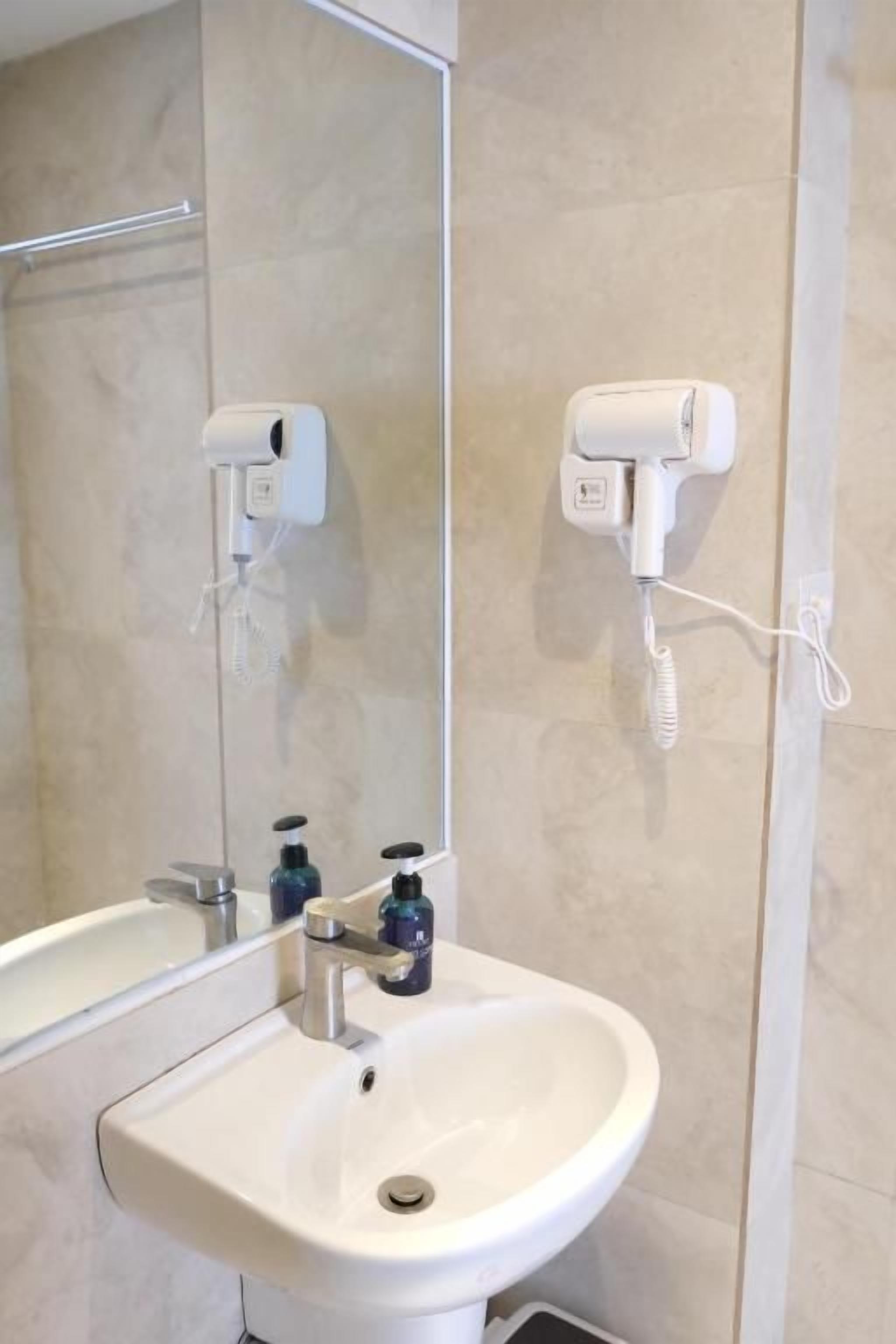 Un baño con un lavabo blanco, un espejo y dos secadores de pelo fijos a la pared.