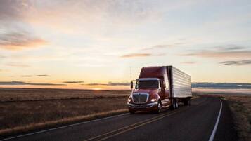 A red semi-truck driving on a road with a sunset in the background.