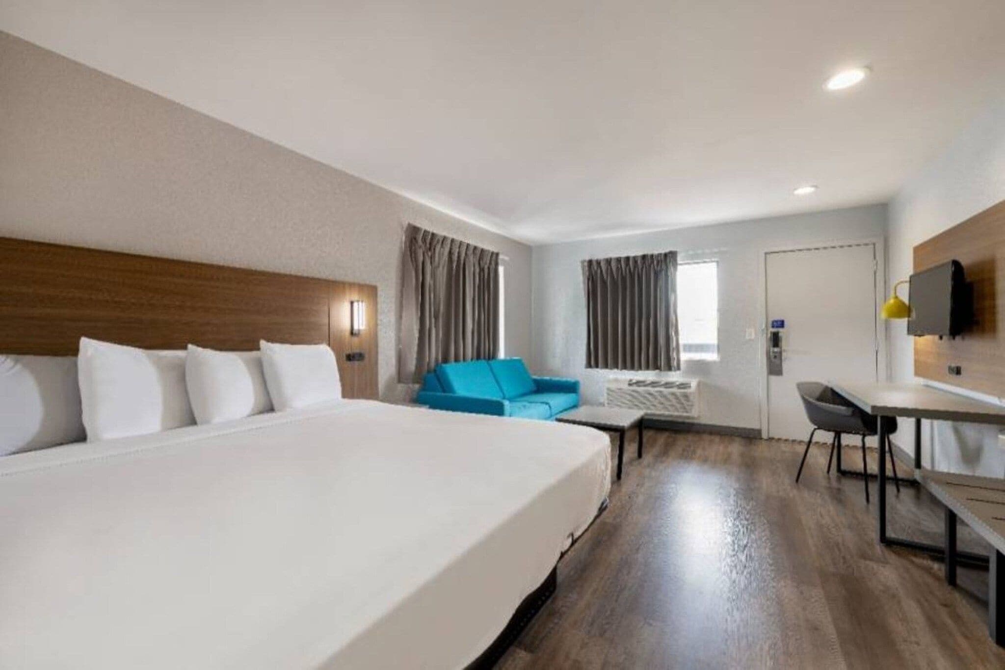 A hotel room with a large bed, a desk, a chair, a blue sofa, and a TV mounted on the wall.