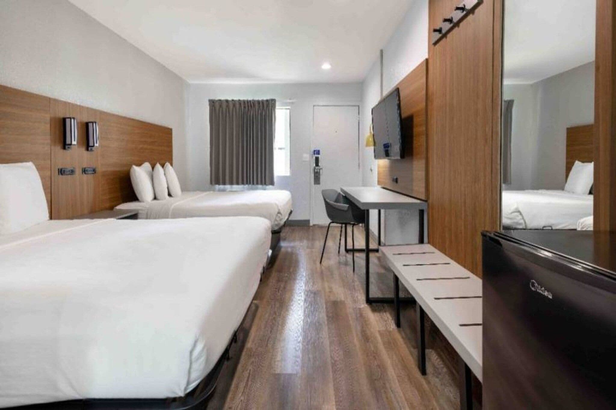 A hotel room with two beds, a desk, a chair, a TV, and a wardrobe.